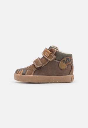 Brun lillebarn sneakers med to velcrolukninger, gummisål og tigerstribemønstre på tå og hæl mod en ensfarvet baggrund.