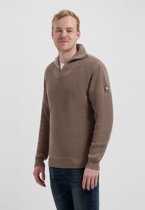 Brauner gerippter Pullover mit einem halben Reißverschlusskragen, langen Ärmeln und einem Knopfdetail an der linken Schulter, getragen über einem weißen Hemd.
