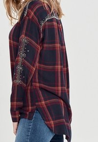 Long-sleeve, navy plaid shirt with red and beige stripes, embellished detailing along shoulders and sleeves; soft, lightweight fabric.