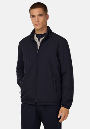 Navyblaue, leichte Jacke mit Reißverschlussfront, Stehkragen, elastischem Bund und Seitentaschen. Glatte, matte Textur, minimales Design.