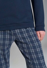 Felpa blu navy con maniche lunghe abbinata a pantaloni grigi a quadri con motivo a scacchi blu e navy, che mette in risalto la texture e il design.