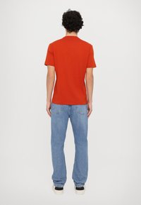 Red short-sleeve t-shirt with a relaxed fit, paired with light blue loose-fitting jeans and black shoes. Simple design, no notable patterns.