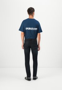Marineblå t-shirt med hvid grafisk tekst, parret med mørk denimjeans. Pasformen er slim, med en standard talje og baglommer.