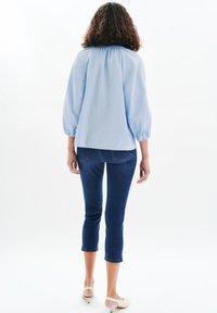 Blusa azzurro chiaro con maniche a sbuffo, abbinata a pantaloni capri in denim scuro. Tessuto morbido e vestibilità ampia; design minimalista.