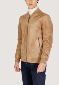 Chaqueta bomber de ante en tono marrón con cierre de cremallera en el frente, puños y dobladillo acanalados. Bolsillo lateral con cierre de cremallera. Textura suave, ajuste moderno.