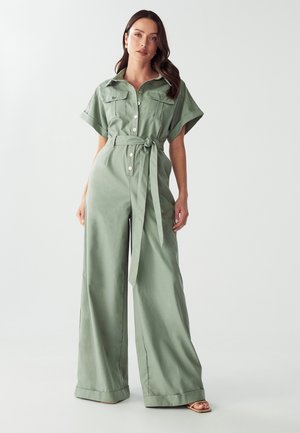 Lichtgroene jumpsuit met korte mouwen, knopen aan de voorkant, twee borstzakken en een tailleband. Heeft een wijde pijp en een zachte textuur.