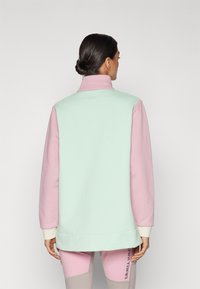 Letefarvet, farveblokeret jakke i mintgrøn og pink, med høj krave, blød tekstur, lange ærmer og en afslappet pasform.