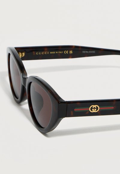 Στρογγυλά γυαλιά ηλίου με σκελετό τύπου χελώνα και σκουρόχρωμους φακούς, με λογότυπο Gucci και πράσινη-κόκκινη-πράσινη ρίγα στα πλαϊνά μπράτσα.