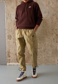 Burgundy hoodie med en framlapp och vit logotyp, tillsammans med strukturerade, ljusgröna cargobyxor med sidofickor och svarta detaljer.