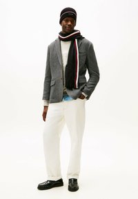 Blazer gris con estampado, suéter crema, pantalones blancos holgados, bufanda negra con acentos rojos, gorro negro y zapatos negros.