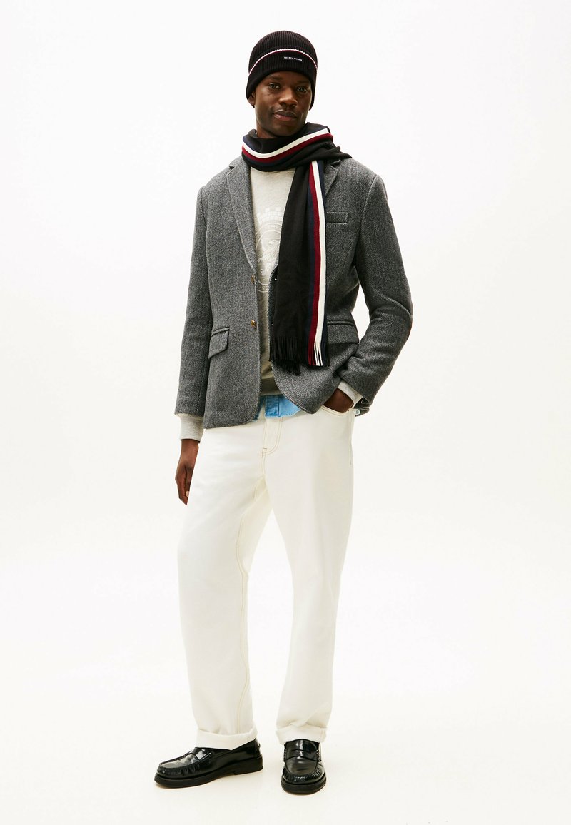 Blazer gris con estampado, suéter crema, pantalones blancos holgados, bufanda negra con acentos rojos, gorro negro y zapatos negros.