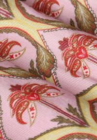 Patterned fabric with pink background, featuring red floral designs, green leaves, and yellow accents. Textured finish with striped details.