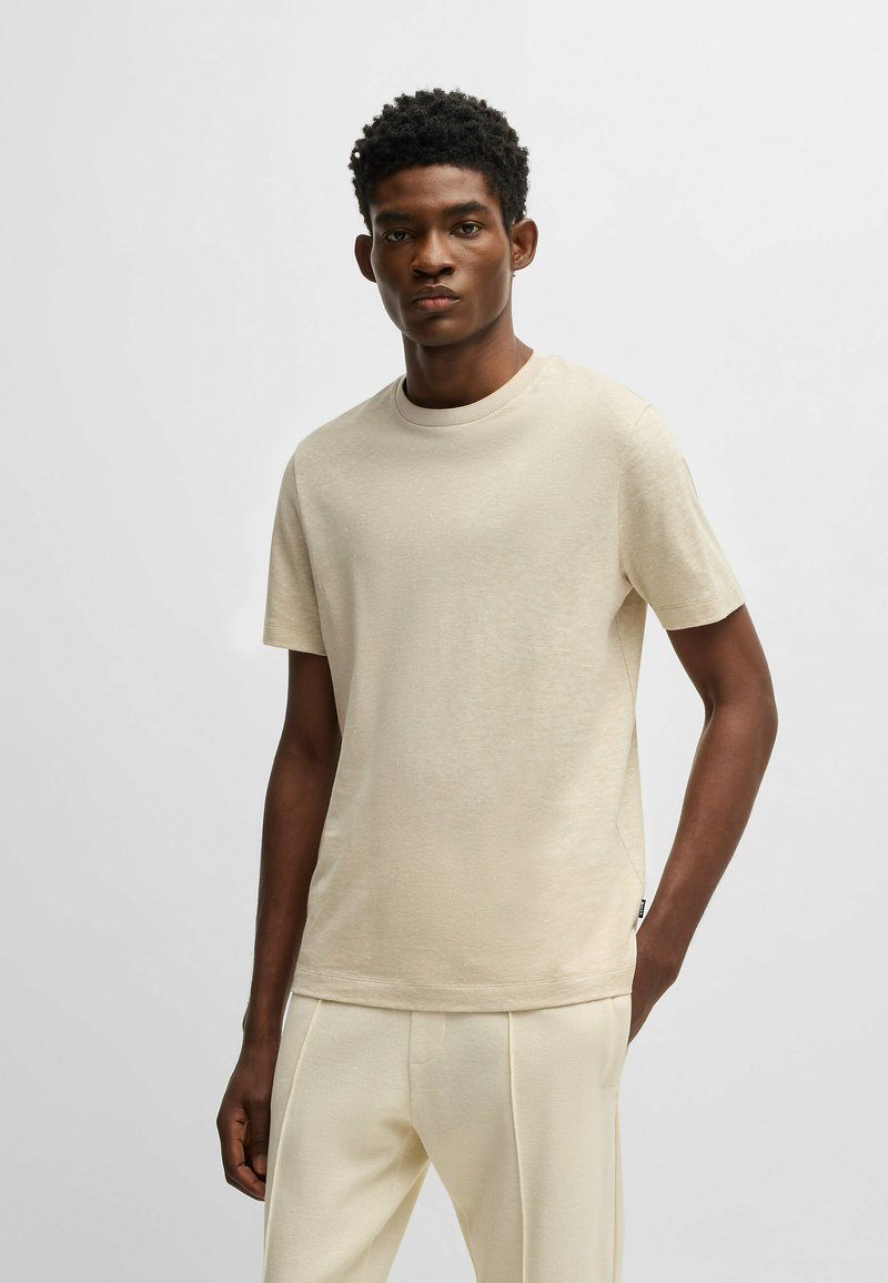 T-shirt beige a maniche corte realizzato in morbido tessuto con scollatura rotonda e vestibilità rilassata, caratterizzato da una texture sottile e dettagli con etichetta laterale.