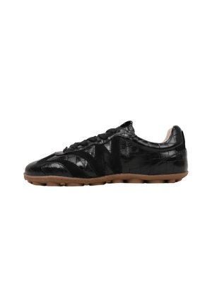 Zapatilla negra de perfil bajo con patrón texturizado, diseño con cordones y suela de goma marrón vista de lado.