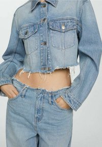 Chaqueta corta de mezclilla azul claro con dos bolsillos delanteros, cierres de botones y bordes deshilachados, combinada con jeans a juego de talle alto.