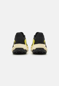 Baskets de sport noires avec des accents jaunes, tige en tissu texturé et semelle en caoutchouc robuste dotée d'un motif nervuré pour une meilleure adhérence.