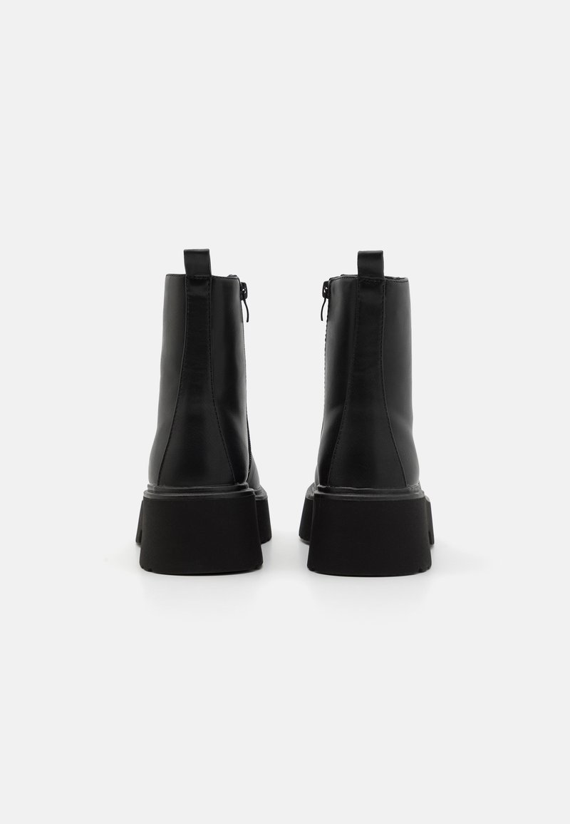 Botas de tobillo de cuero negro con textura suave, cierre de cremallera y suela de plataforma negra resistente. Cuenta con una tira de bucle para una fácil colocación.