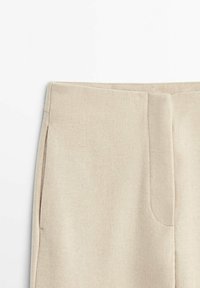 Beige high-waist pants with a front seam and side pockets, made from a soft textured fabric.