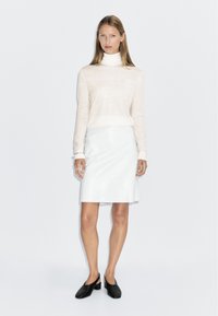 Pull à col roulé beige clair associé à une jupe en cuir blanc ajustée et des chaussures à talons blocs noires ; design minimaliste et épuré.