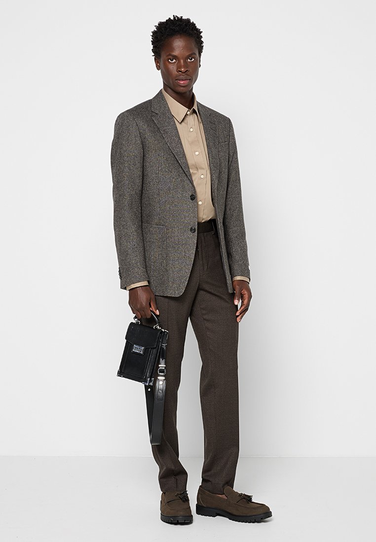 Grau meliertes Blazer mit dezenten Mustern, beiges Hemd mit Knöpfen, braune Hose, schwarze Tasche und braune Schnürschuhe.