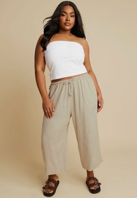 Lichte beige wijde broek met een elastische tailleband en drawstring, gecombineerd met een witte strapless top. Platte sandalen maken de outfit compleet.