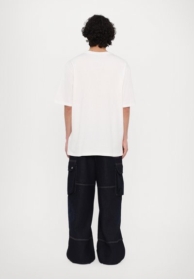 Λευκό T-shirt από βαμβάκι με κοντά μανίκια, σε συνδυασμό με χαλαρά μπλε τζιν cargo παντελόνια με πολλές τσέπες και αντίθετη ραφή.
