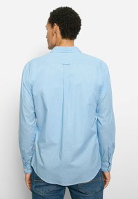 Hellblaues Langarmhemd aus gewebtem Stoff mit Button-Down-Kragen, abgerundetem Saum und einfacher Rückenfalte für eine gute Passform.