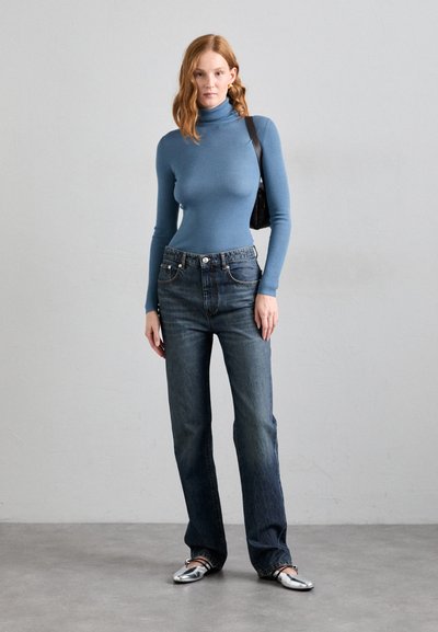 Ribbed blue turtleneck top, high-waisted dark denim jeans, and silver flats; model accessorized with a black shoulder bag.