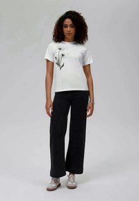 White t-shirt with black floral print, paired with wide black jeans. Model wears light sneakers. Simple design and relaxed fit.