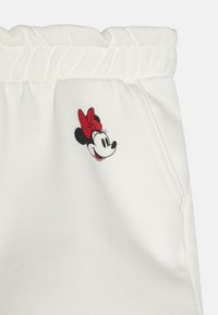 Baltas kokvilnas sporta bikses ar elastīgu jostu un sarkanu Minnie Mouse grafiku uz gurniem. Mīksta tekstūra ar kabatām.