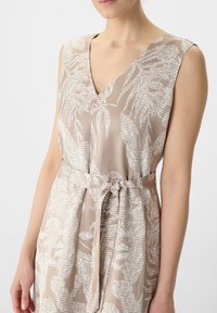 Sukienka bez rękawów w beżowym materiale z białymi wzorami liści, z głębokim dekoltem w kształcie V i wiązaniem w pasie, umożliwiającym regulację dopasowania.
