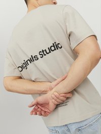 Béžové bavlněné tričko s krátkými rukávy a potiskem "Originals Studio" na zádech. Lehká tkanina s volným střihem.