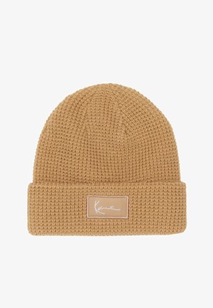 Gorro de punto en un cálido color marrón claro, con una tela texturada y un dobladillo doblado que presenta un parche rectangular de logotipo en beige claro.