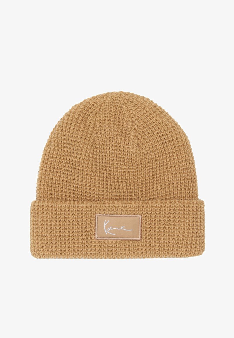 Meleg bézs színű kötött sapka, texturált anyagból, hajtott párnával és világosbézs színű, téglalap alakú logópacsival.