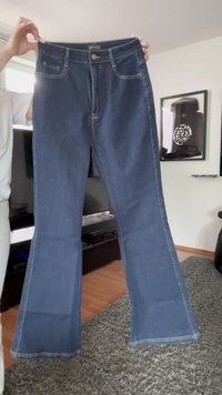 Jeans de campana azul oscuro con acentos cosidos, bolsillos frontales y cremallera delantera. La tela tiene una textura suave y un aspecto clásico de mezclilla.