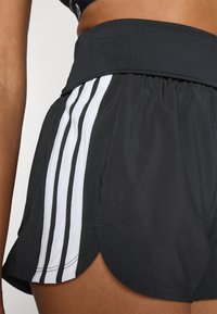 Sorte treningshorts med bredt liv, med tre vertikale hvite striper på siden og en svakt buet kant. Glatt tekstur.