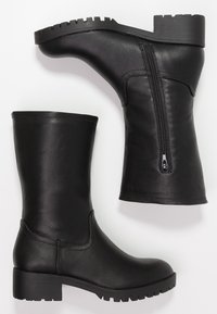 Botas de cuero negras a medio gemelo con cremallera lateral, puntera redonda, tacón bajo grueso y suela con relieve, mostradas sobre fondo blanco.