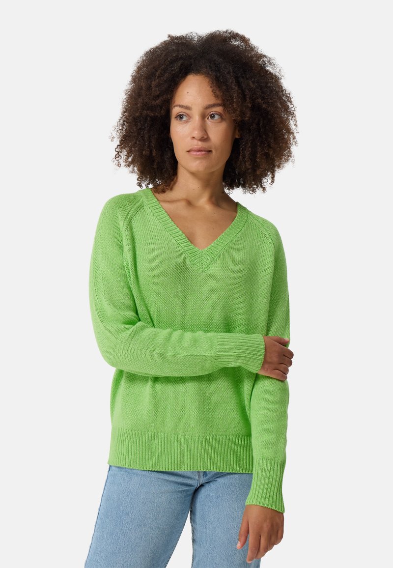 Groene V-hals trui met een losse pasvorm, lange mouwen, ribgebreide manchetten en zoom. Geweven textuurpatroon. Gepaard met lichtblauwe jeans.
