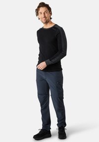 Black long-sleeve shirt with dark gray accents; paired with dark blue cargo pants featuring zippered pockets. Black sneakers complete the look.