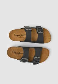 Schwarze Sandalen mit doppeltem Riemen, Metall-Schnallen und braunen, gepolsterten Innensohlen mit der Marke "Pepe Jeans London", von oben auf einem grauen Hintergrund dargestellt.