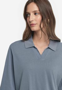 Ljusblå V-ringad polo t-shirt med krage och texturerat tyg. Lätt passform med lång ärm, vilket ger en avslappnad och ventilerande design.