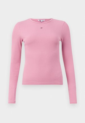 Langärmliges, geripptes T-Shirt in Hellrosa mit Rundhalsausschnitt und einem kleinen Logo-Detail auf der Brust. Weicher Stoff, körperbetonte Silhouette.