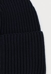 Berretto a maglia di colore blu scuro, con texture a costine. Il design include un risvolto per un fit regolabile e maggiore calore.