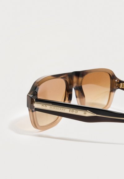 Καφέ σκουρόχρωμα ορθογώνια γυαλιά ηλίου με διαφανές καφέ πλαίσιο και μαύρους βραχίονες που φέρουν χρυσή λεπτομέρεια με το λογότυπο Burberry.