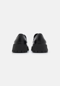 Black leather shoes with a thick, textured rubber sole featuring deep grooves. The design is low and rounded at the back.
