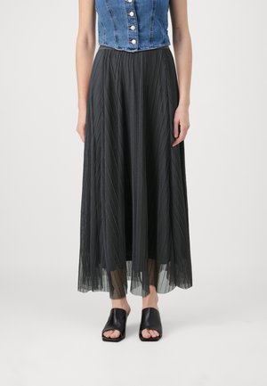 Zwarte geplooide maxi-rok met een doorschijnende overlay, gecombineerd met een denim crop top. Model draagt open teen zwarte slip-on schoenen.