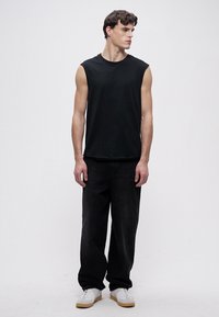 Black sleeveless t-shirt, paired with loose-fitting black jeans and white sneakers, set against a plain white background.