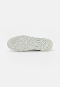 Semelle blanche en caoutchouc de chaussure de sport avec une prise texturée, présentant un motif circulaire et des lignes en relief. Logo Lacoste embossé près du talon.
