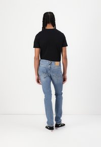 Tajtat svart t-shirt och ljusblå jeans. Jeansen har en läderlapp på baksidan och klassisk femficksdesign. Svarta sneakers.