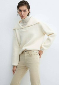 Crème oversized trui met een col, gecombineerd met beige aansluitende jeans. Zachte gebreide textuur met een ontspannen silhouet.
